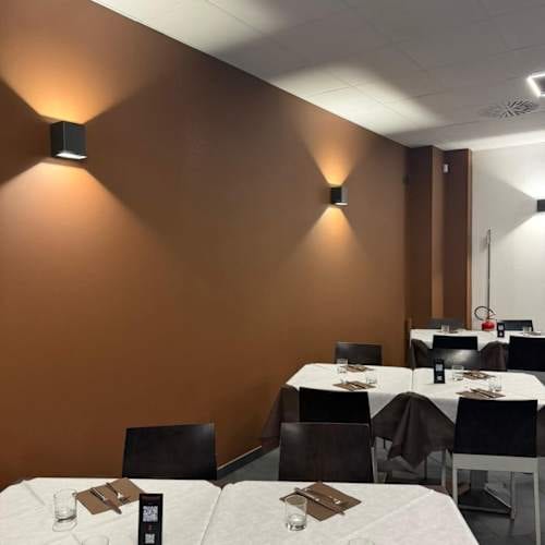 La sala di RistorAntò: parete marrone con lampade a cubo che spandono luce verso l'alto e verso il basso, tavoli con tovaglie bianche